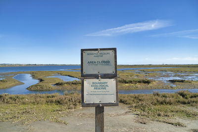 Information sign on field by lake against sky