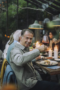 Smiling senior man holding wineglass while sitting at dining table during party