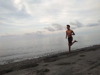 Full length of shirtless man running at beach against sky