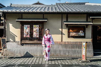 Woman wearing kimono while standing on street against building