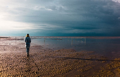 Rear view of man walking on beach against sky