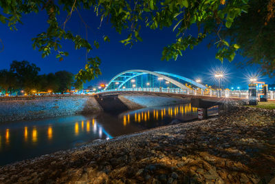 Illuminated bridge over river against sky at night
