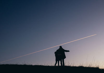 Silhouette of two people above a cliff in the evening