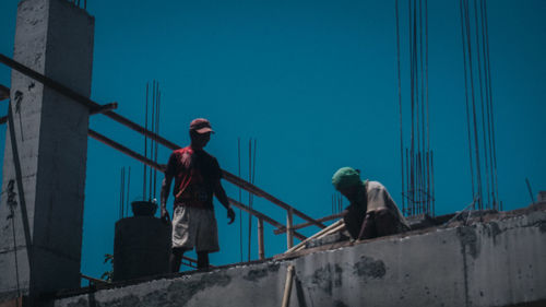 Low angle view of worker working at construction site against clear blue sky