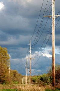 Electricity pylon on field against cloudy sky