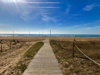 Boardwalk leading towards sea against sky