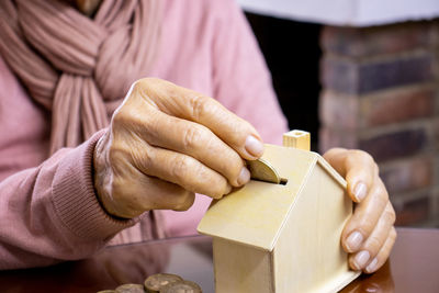 Midsection of senior woman inserting coin in piggy bank