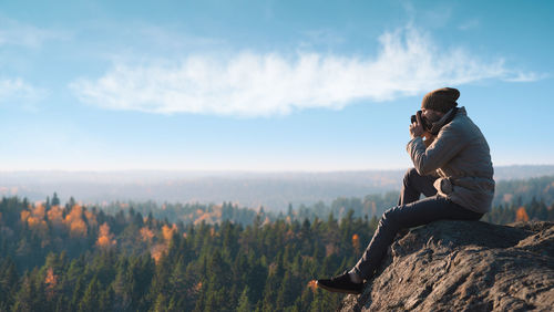 Man sitting on rock against sky