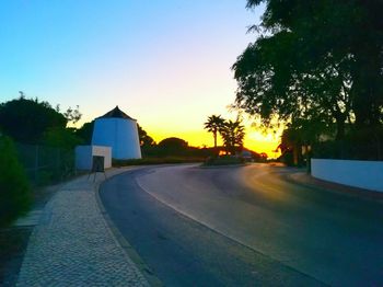 Road by trees against clear sky during sunset