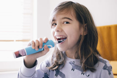 Happy girl with brown hair brushing teeth at home