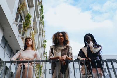 Low angle view of young women standing by railing against sky