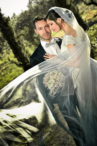 Portrait of bridegroom standing with bride against trees