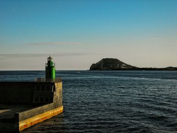 Lighthouse by sea against clear sky