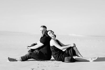 Young couple sitting on beach against sky