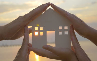 Cropped image of family holding house shape at beach during sunset