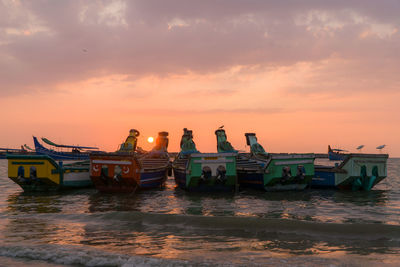 Boats moored in sea against sky during sunset