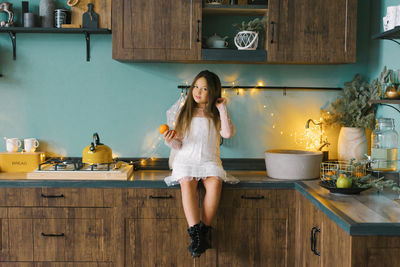 A beautiful girl of seven years old is sitting in the kitchen and holding tangerines in her hands