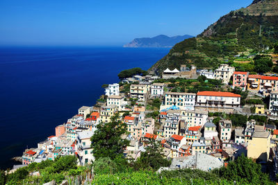 Buildings on mountain at manarola by sea against clear blue sky