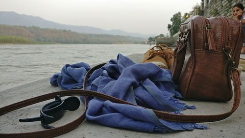 Close-up of bag by shawl and hair pin at riverbank