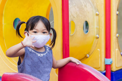 Portrait of girl wearing mask sitting on slide