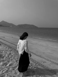 Rear view of woman standing at beach against sky