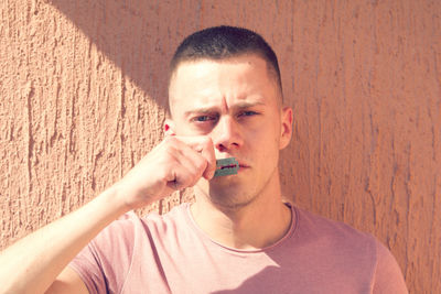 Portrait of young man holding razor blade against wall