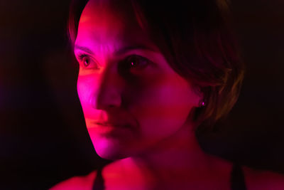 Close-up portrait of a young woman illuminated by stripes of pink and red,  viva magenta neon light