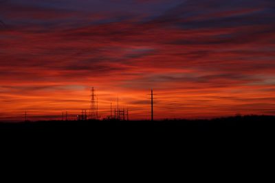 Silhouette electricity pylon on field against dramatic sky during sunset