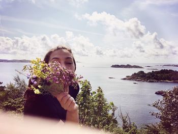 Woman holding flowers at beach against sky