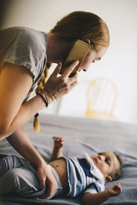 Mother dressing toddler while talking on mobile phone at home