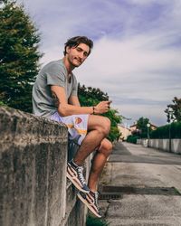 Young man sitting on retaining wall against sky