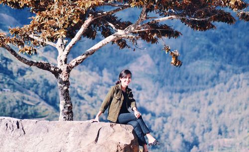 Woman sitting on tree against mountain