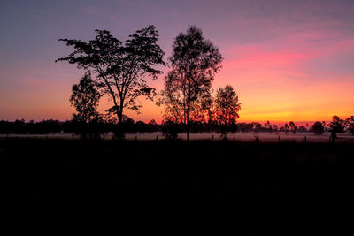 Silhouette trees on field against romantic sky at sunset