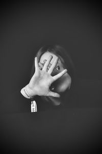 Portrait of a woman covering face over black background