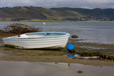 Boat moored on shore by lake against sky