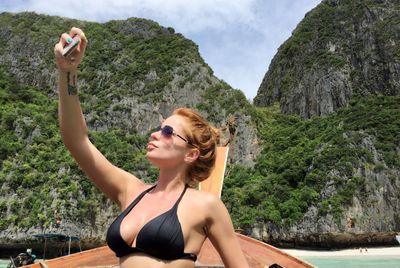 Young woman in longtail boat against rocky mountains taking selfie at phi phi islands