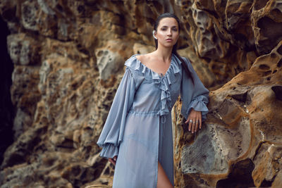 Fashionable brunette woman in a gray dress stands on a cheese rock in the summer