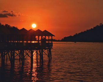 Silhouette house by sea against orange sky