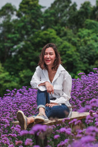 Portrait of smiling woman sitting on purple flowering plants