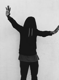 Man with arms outstretched wearing hood while standing against wall