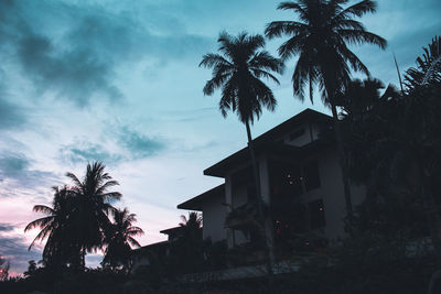 Silhouette palm trees by building against sky at sunset