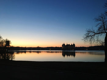 Silhouette trees by lake against clear sky during sunset