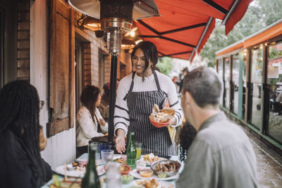 Smiling waitress talking to family having food at restaurant