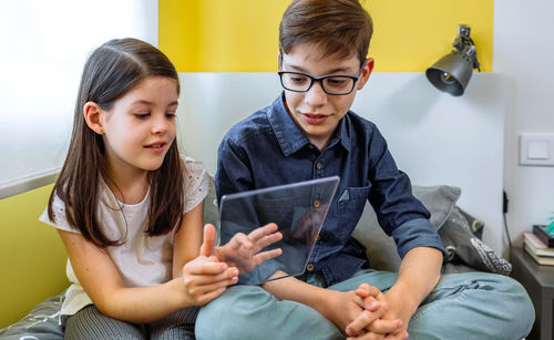 Happy children having fun with futuristic transparent tablet sitting over bed.