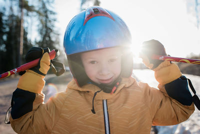 Close up of a young boy wearing a ski helmet holding poles at sunset