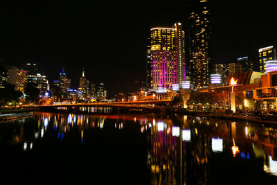 Illuminated buildings by river against sky at night