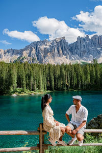 People sitting by lake against mountains