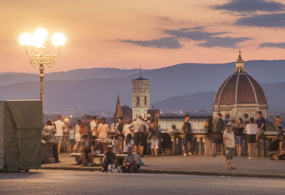 People at illuminated city against sky during sunset