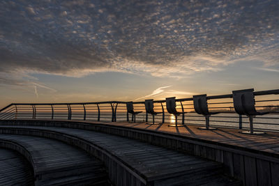 Empty chairs on promenade against sky during sunset