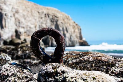 Close-up of rusty metal on rock against sky